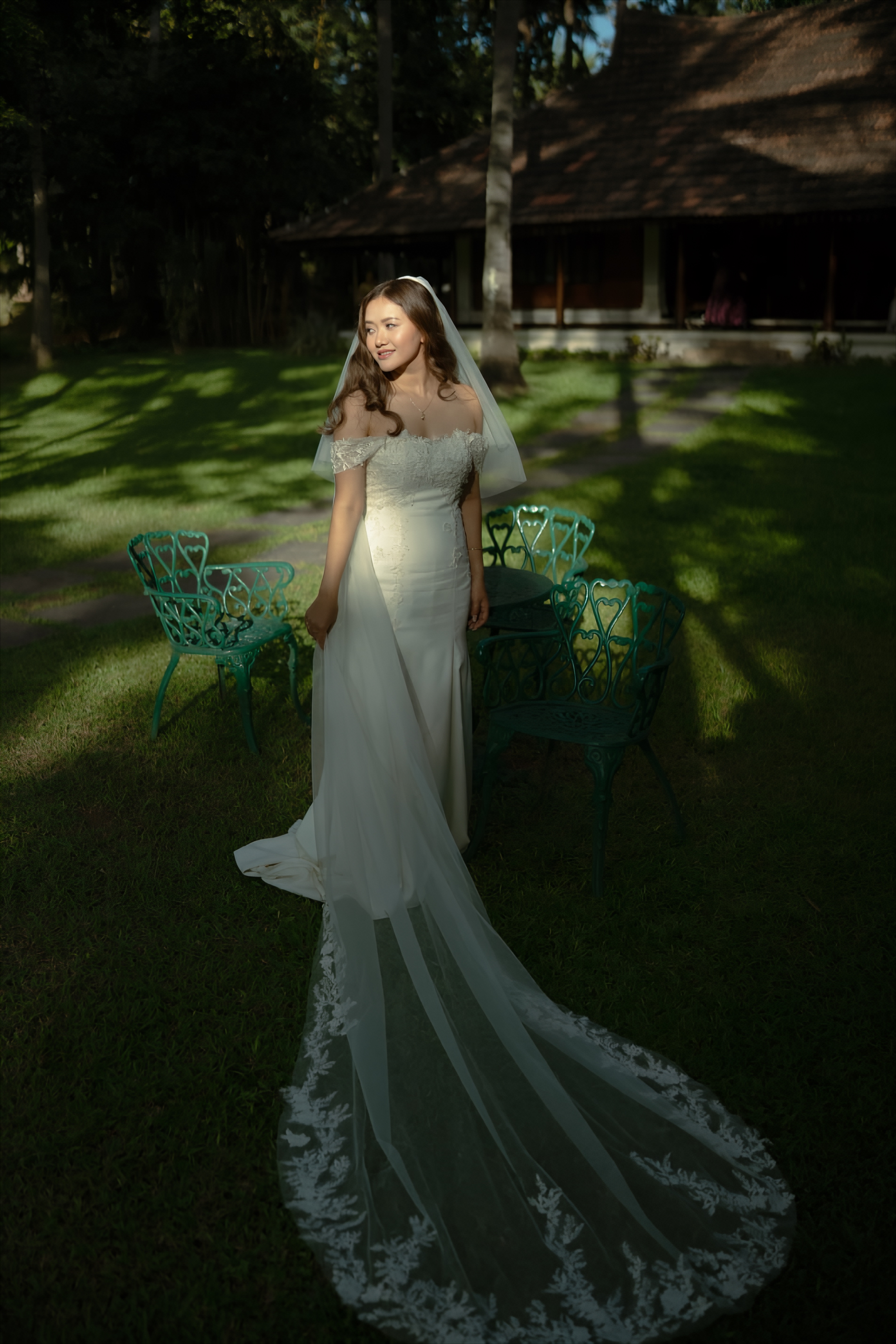 Bride in a white dress standing in a garden as afternoon light crosses the scene