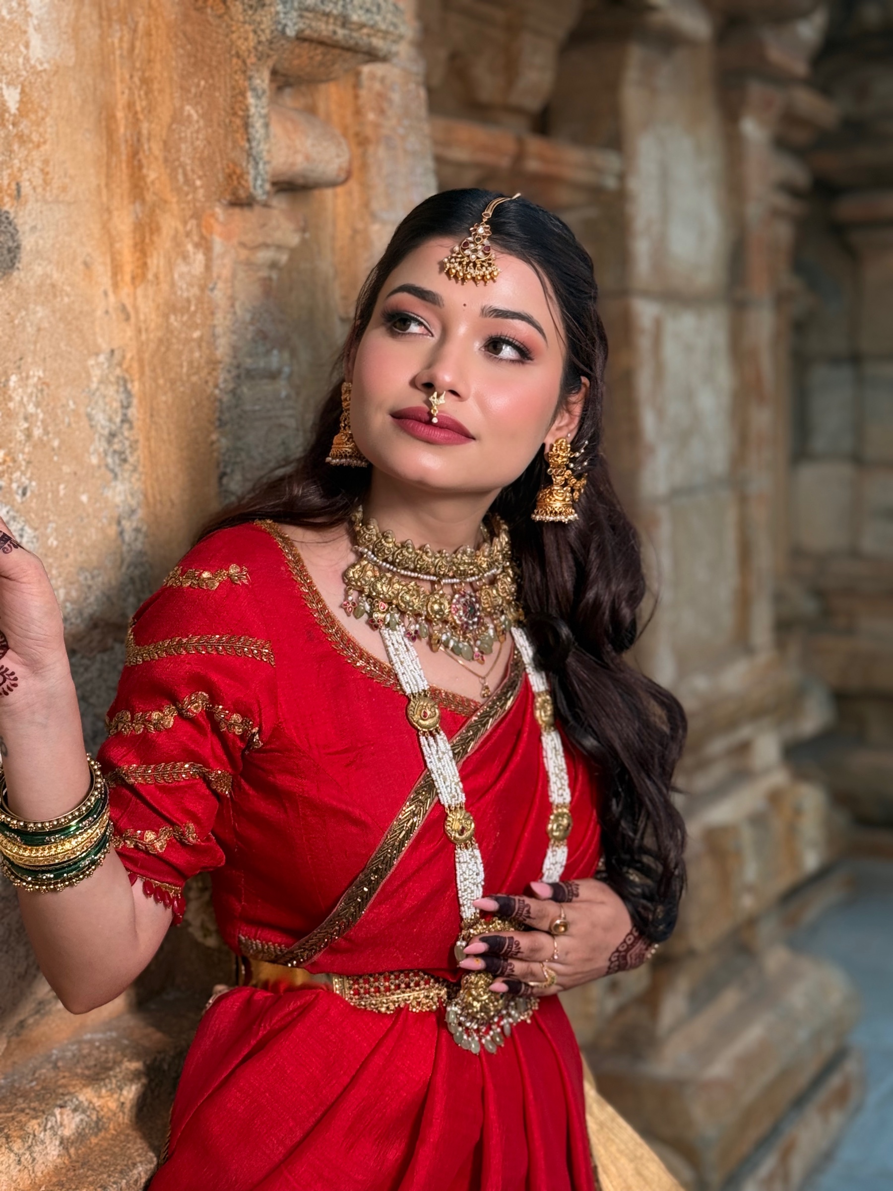Bride in a red sari posed against carved temple stone