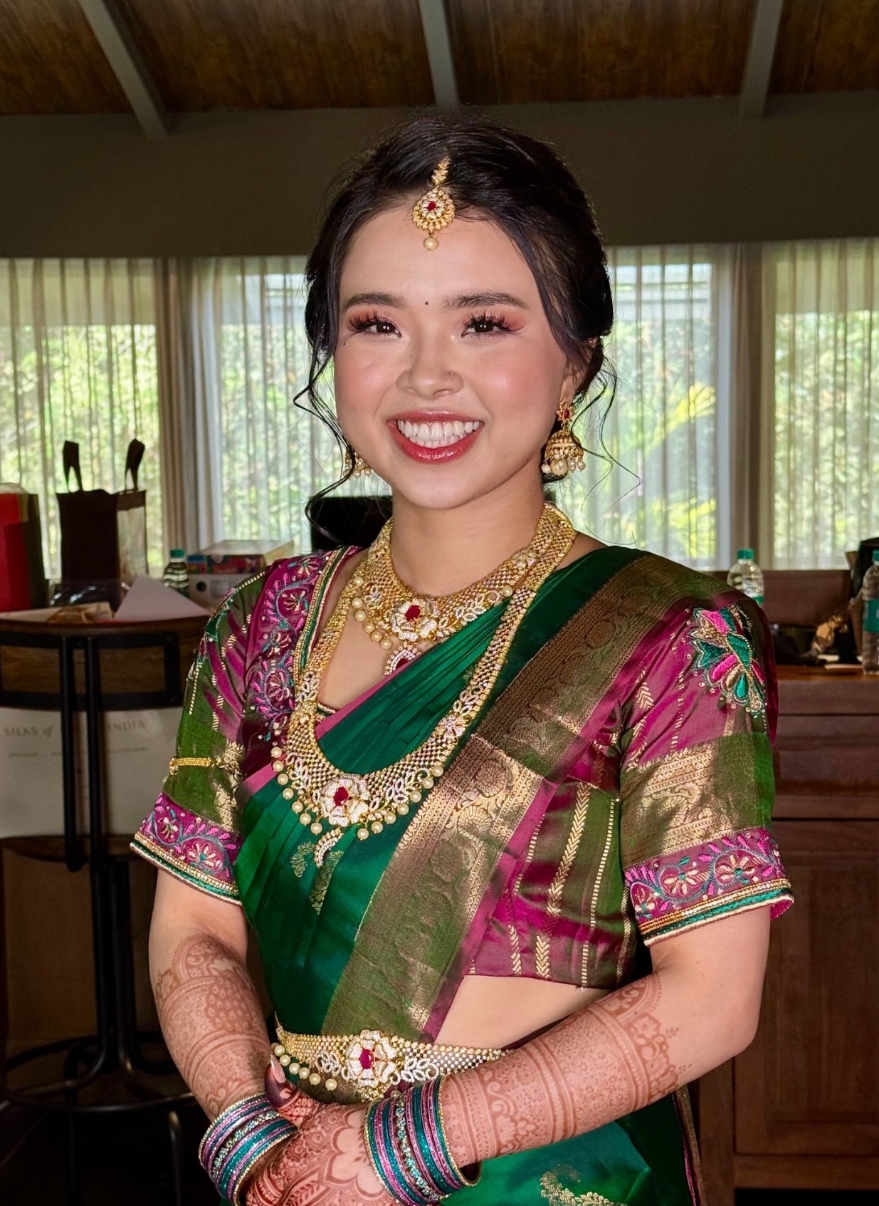 Bride smiling in an emerald and magenta sari with jasmine in her hair